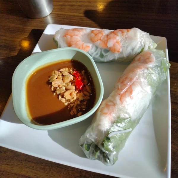 Two fresh spring rolls with shrimp and a side of peanut sauce with crushed peanuts and chili.