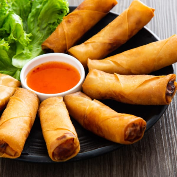 Crispy golden spring rolls with a side of sweet chili dipping sauce and fresh lettuce.