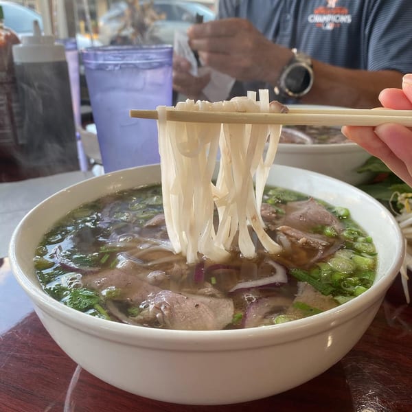 Chopsticks lifting pho noodles from a steaming bowl of Pho 9's beef pho.