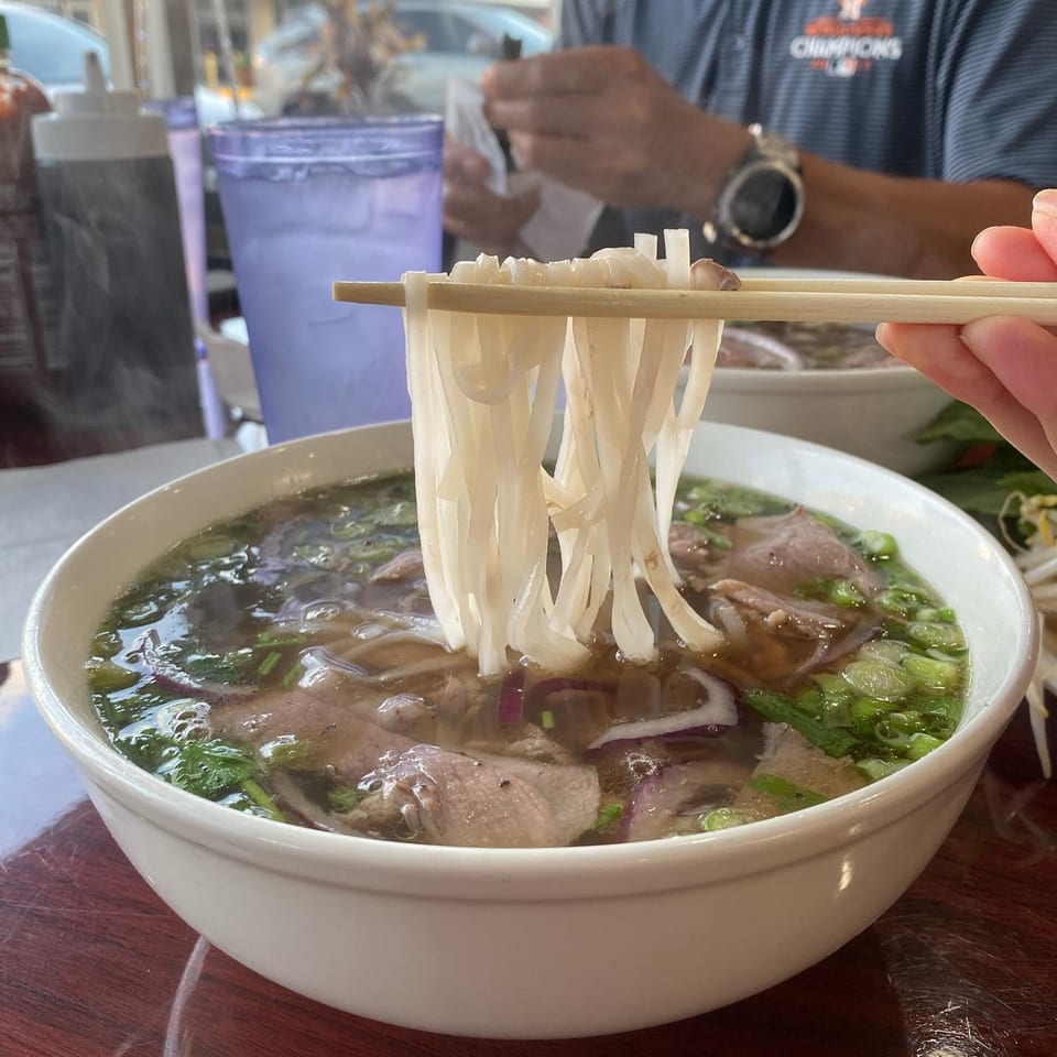 Chopsticks lifting pho noodles from a steaming bowl of Pho 9's beef pho.