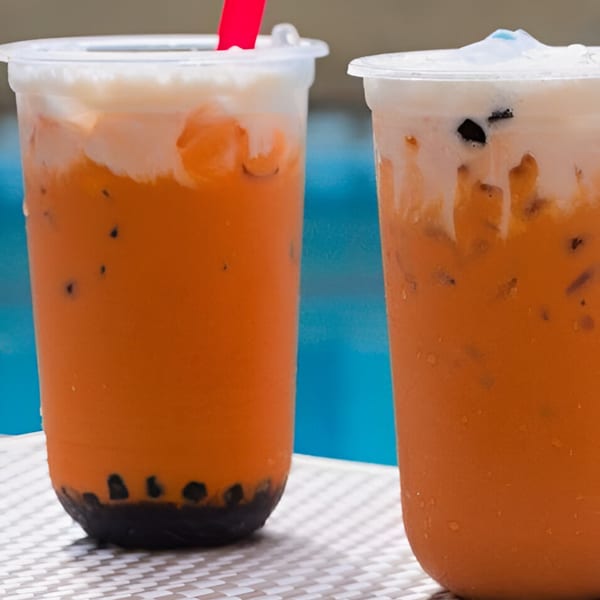 Two plastic cups of Pho 9's iced Thai tea with boba and creamy topping on a white table.