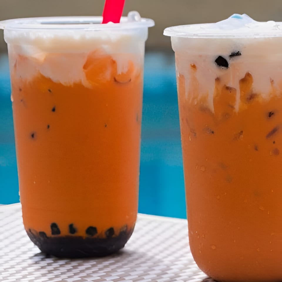 Two plastic cups of Pho 9's iced Thai tea with boba and creamy topping on a white table.